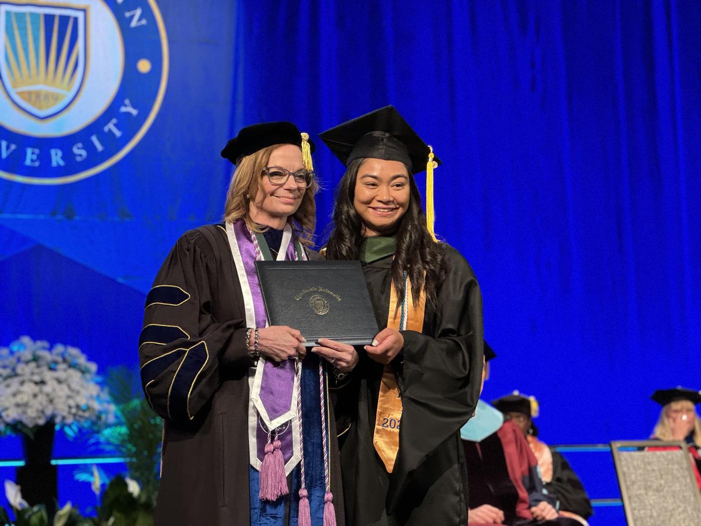 Graduate receiving their diploma posing with a faculty member