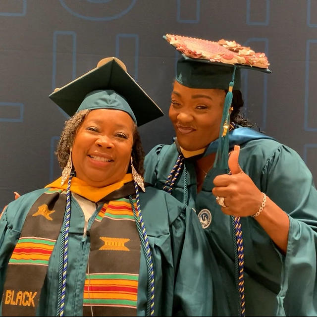 A person in graduation gowns and cap and gowns giving a thumbs up