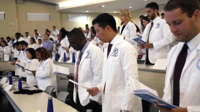 students in white coat read oath