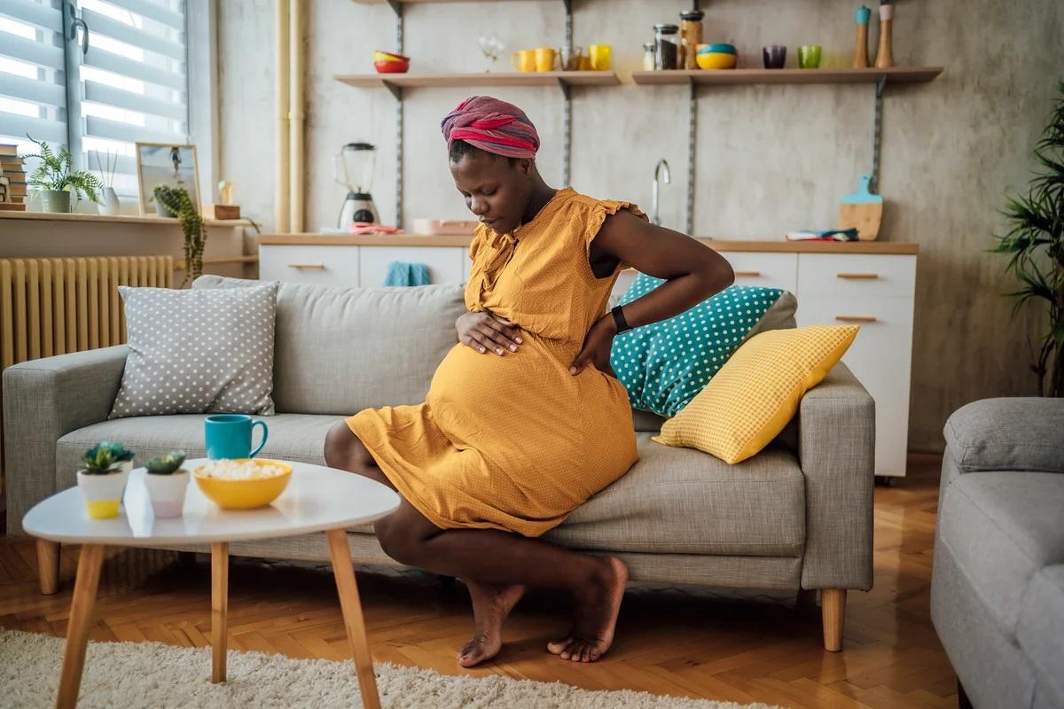 Pregnant woman patting her stomach while sitting on the sofa in a sunny living room