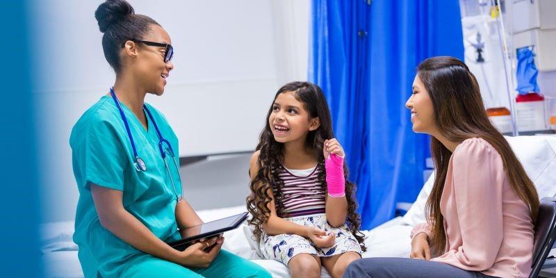 A nurse sitting with her young patient and their mother