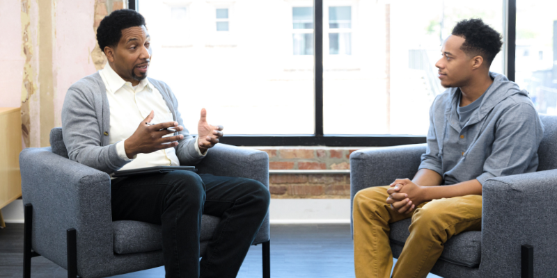 Two men sitting in chairs facing each other having a conversation.