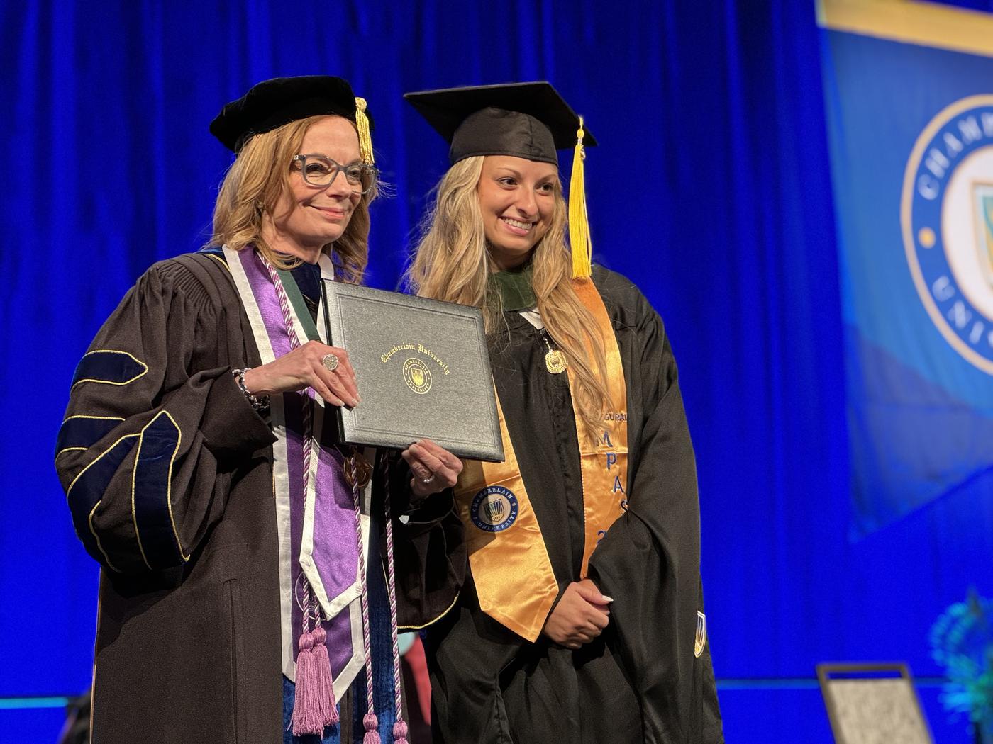 A graduate posing with faculty holding diploma
