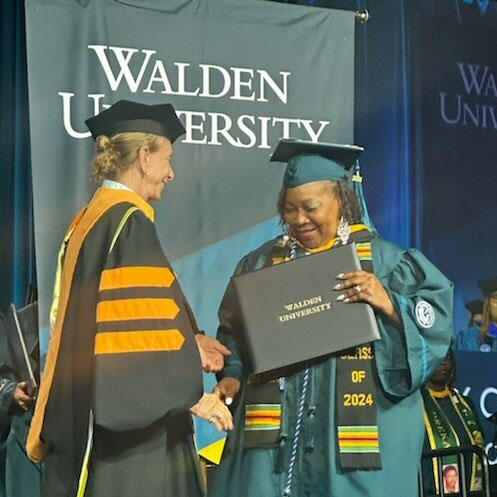 A person in graduation gowns holding a diploma