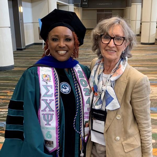 Two female alumni standing with faculty at graduation