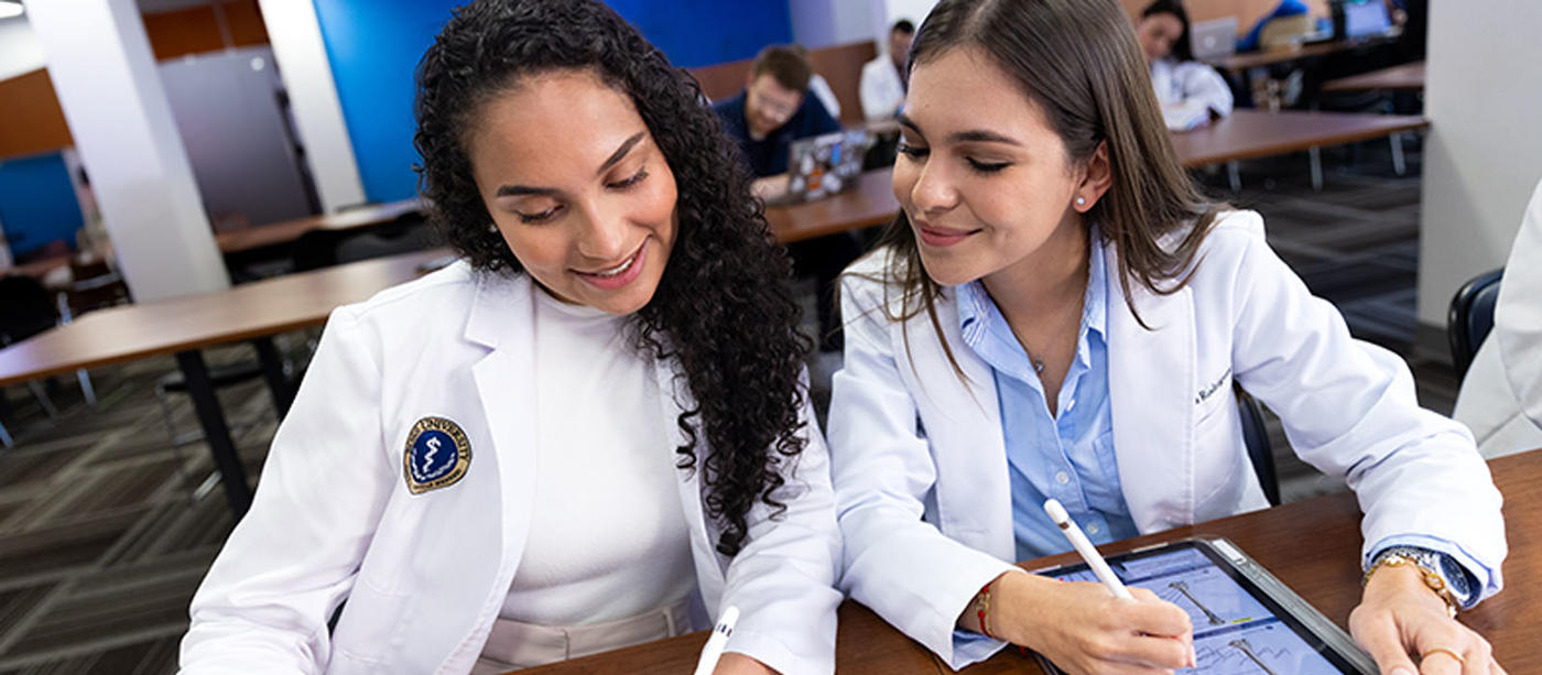 two women in lab coats looking at a tablet