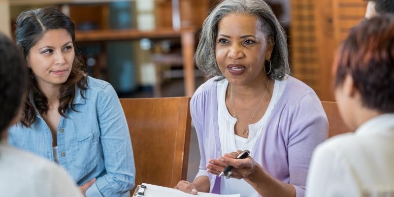 Woman speaking to other women at a table.