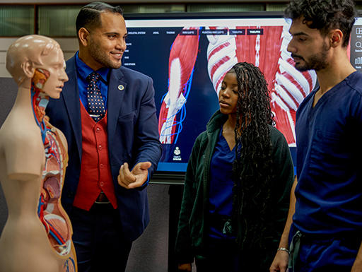 Instructor speaking to two medical students in blue scrubs
