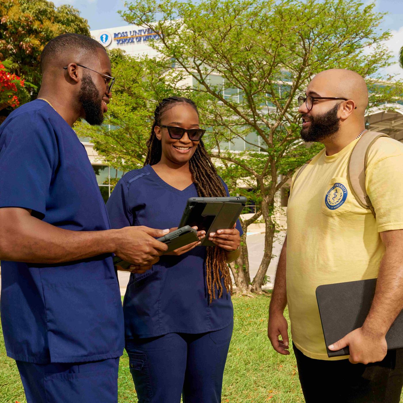 Two Ross Med students in blue scrubs and one in yellow t-shirt in front of building