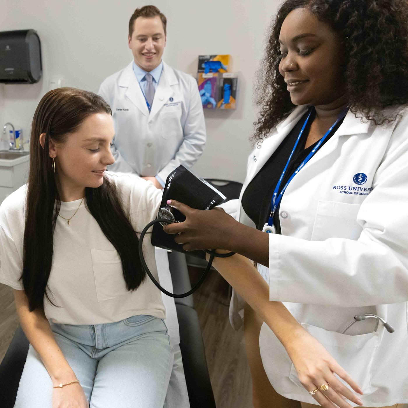 Two medical professionals in lab coats and one checking patient blood pressure