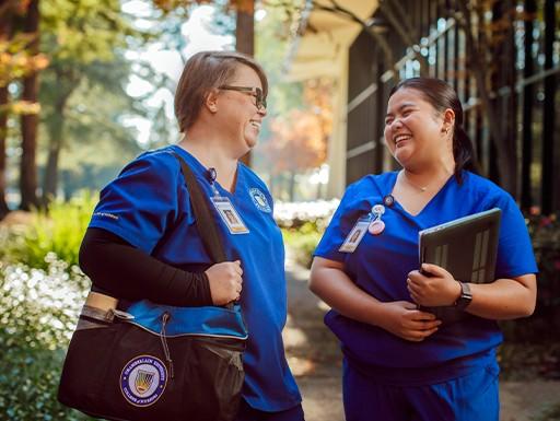 Two medical students wearing blue scrubs outside a building 