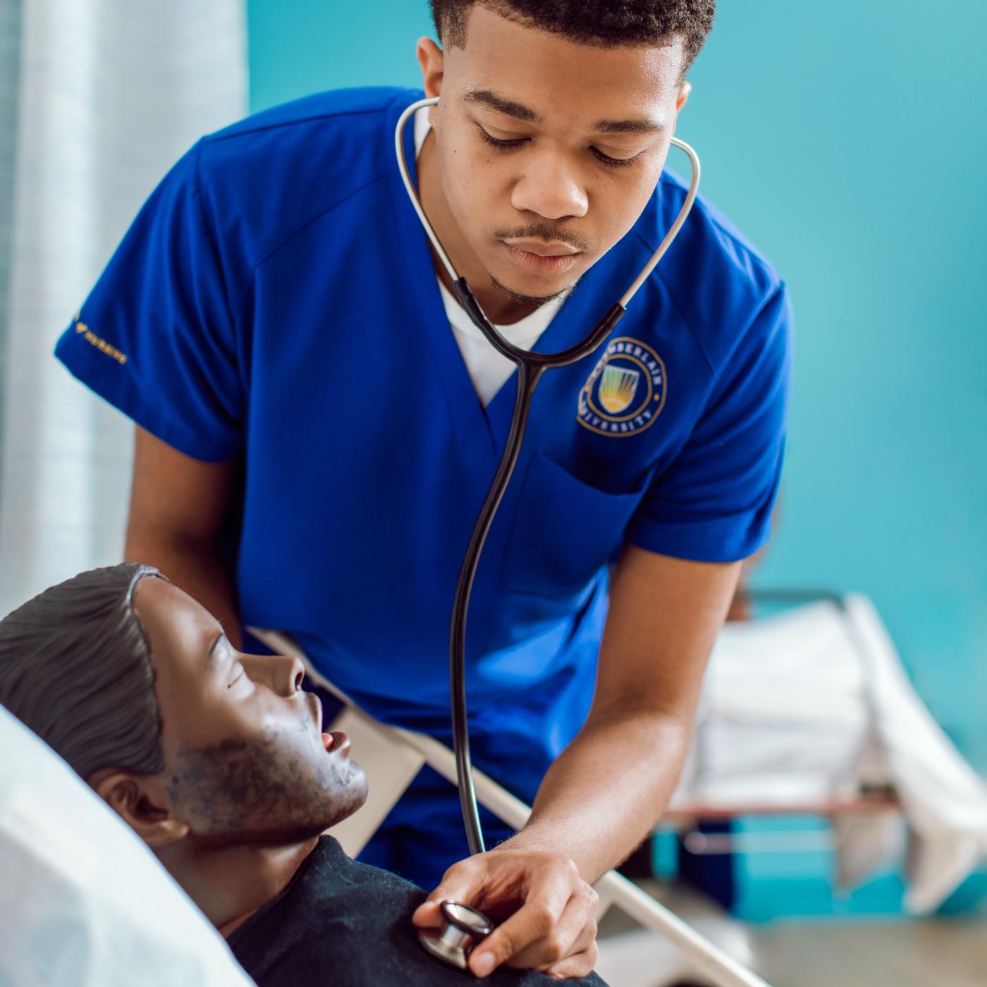 Male nurse in blue scrubs doing training on a mannequin