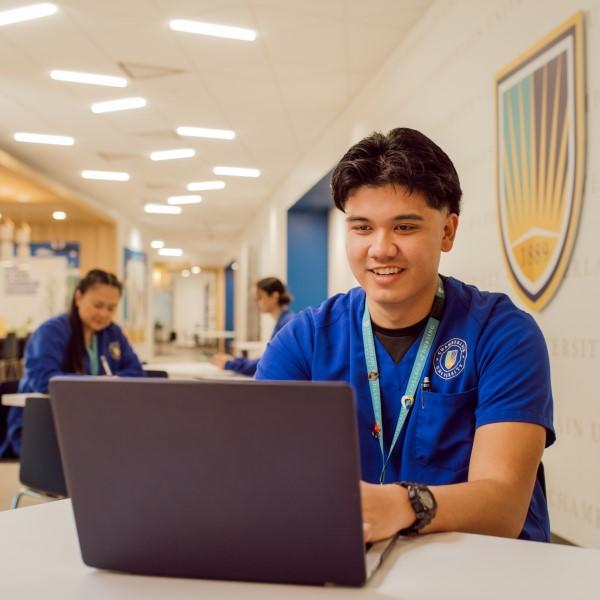 male in blue scrubs on a laptop