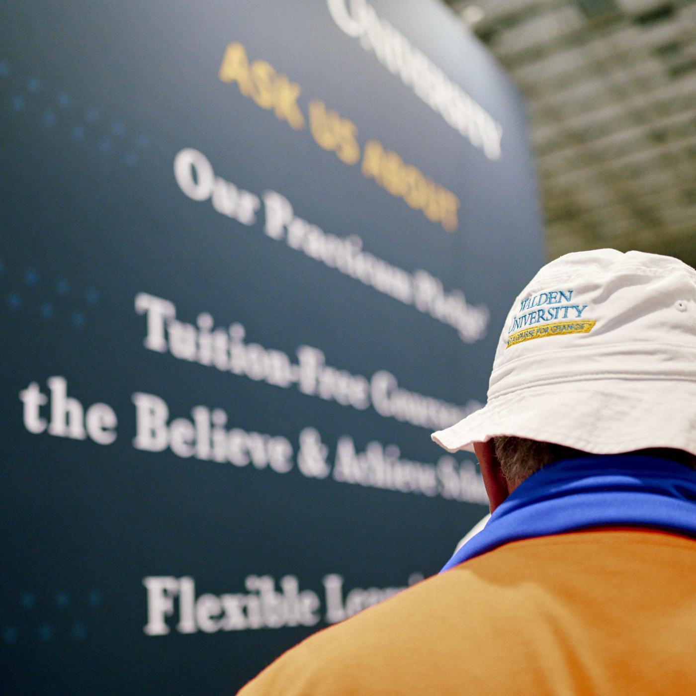 back of man wearing a Walden University hat next to a banner