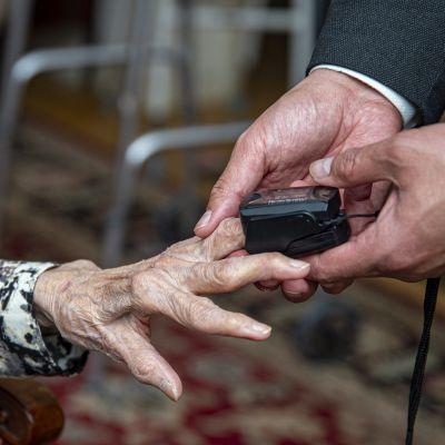 Elderly woman's hand with pulse monitor being placed on it.