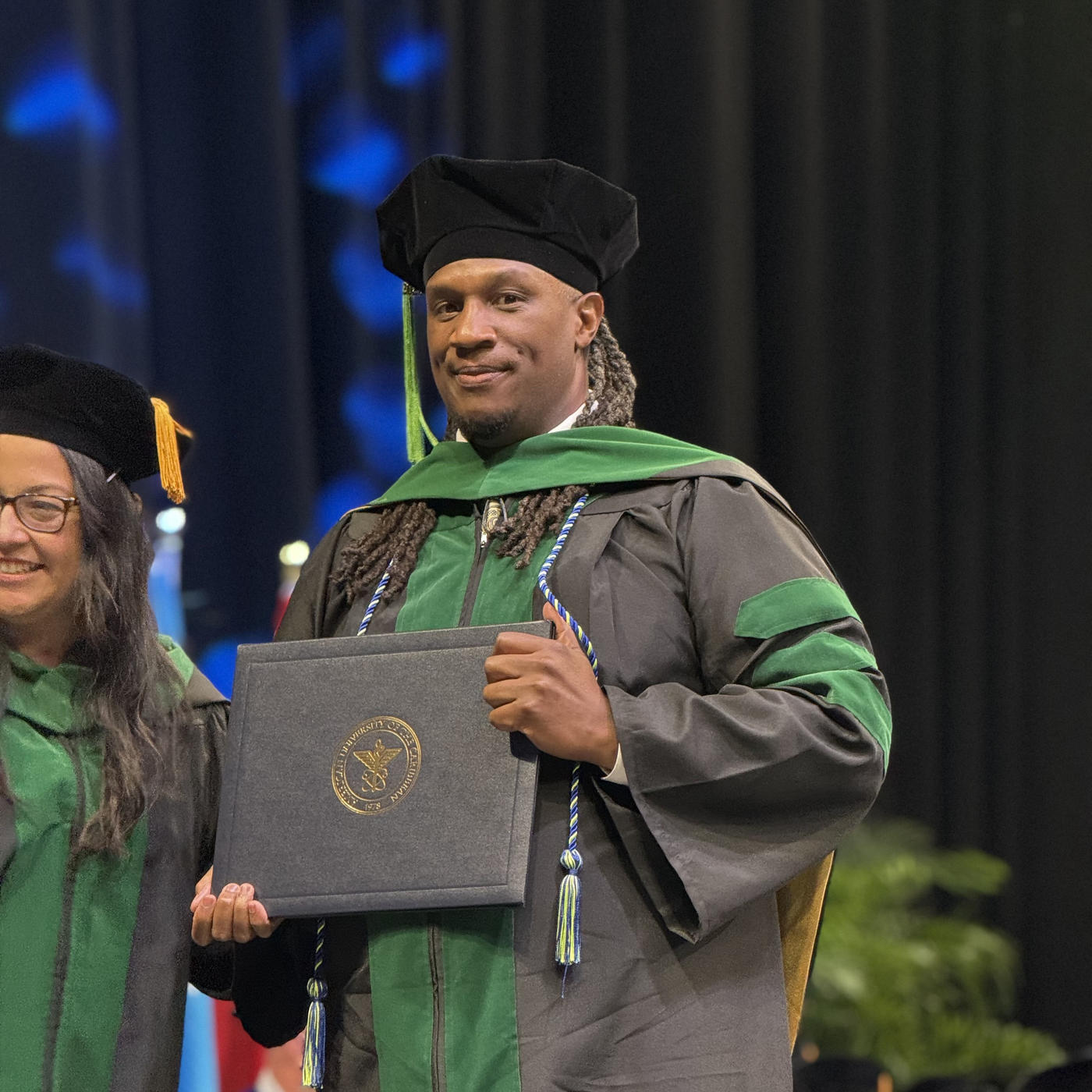 Cliff Davis in graduation regalia on stage holding diploma
