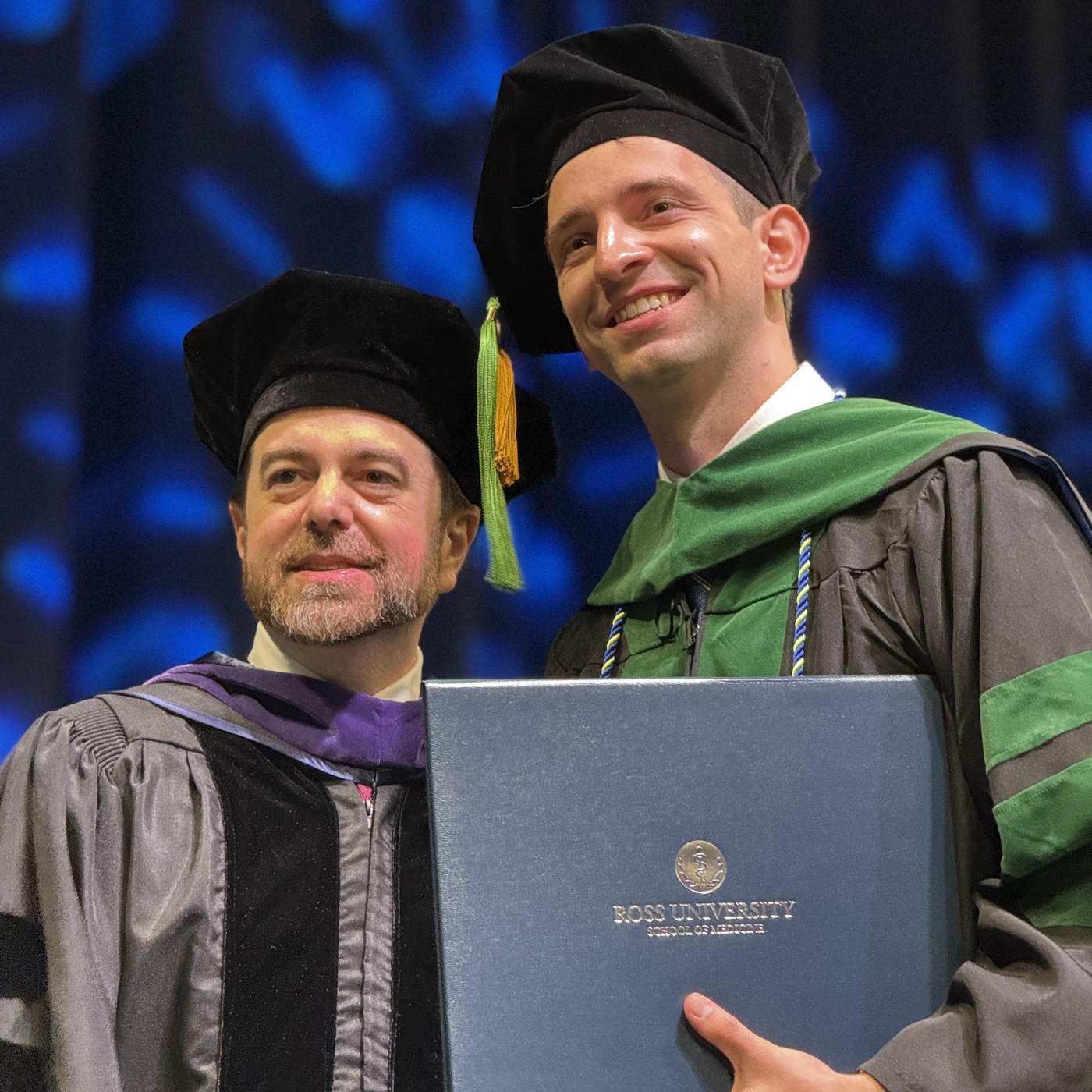 Zac Petrucci in graduation regalia on stage holding diploma